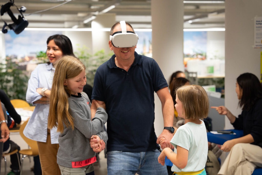 Ein Vater mit VR-Brille wird von seinen 2 Kindern geleitet.