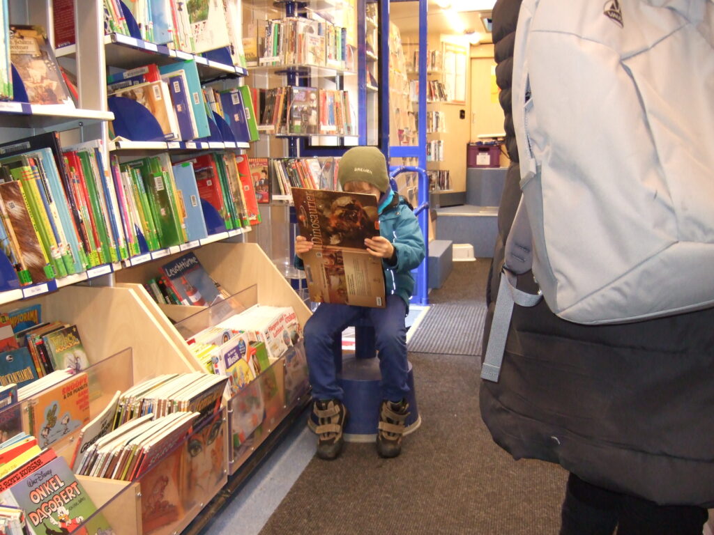 Ребенок читает книгу о динозаврах в автобусной библиотеке.