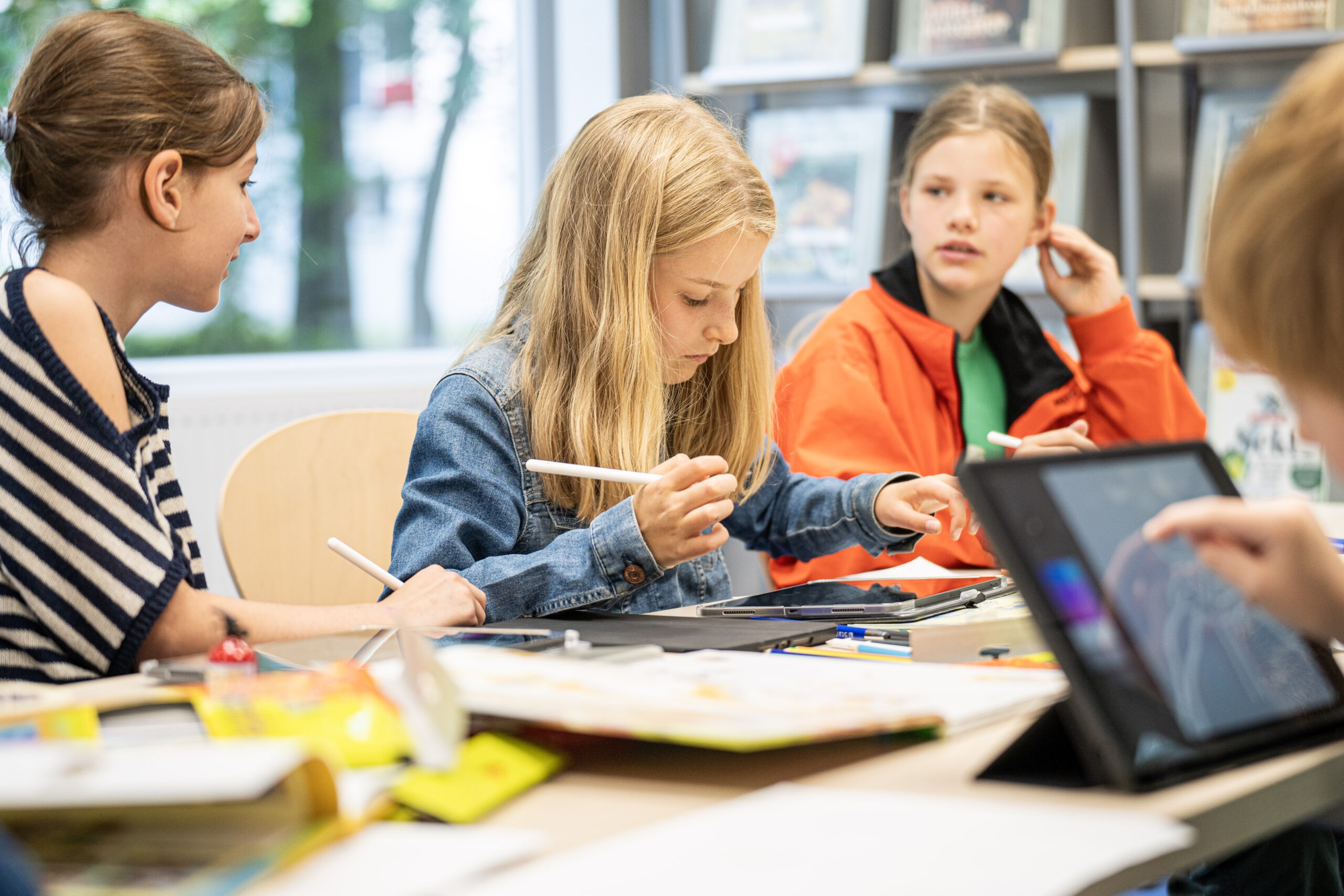 Drei Mädchen sitzen an einem Tisch und zeichnen auf Tablets.