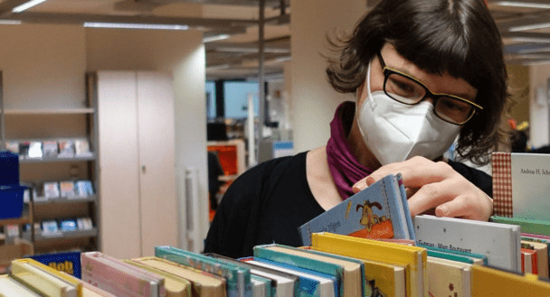 FFP2 maskesi takan bir kadın kitap rafında duruyor.