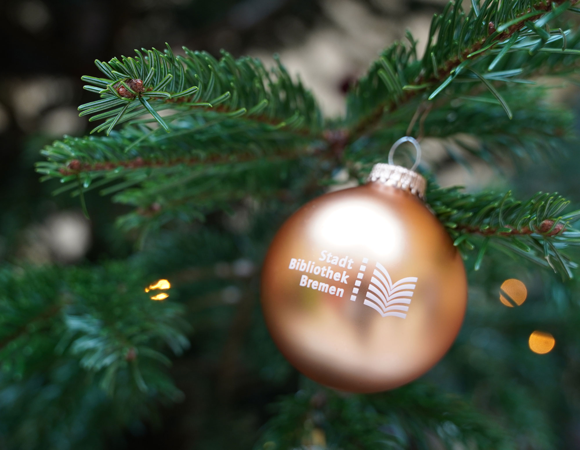 Eine Weihnachtsbaumkugel mit dem Schriftzug Stadtbibliothek Bremen hängt an einem Tannenbaum.