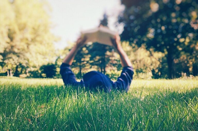 Bir kişi çayırda uzanır ve kitap okur.