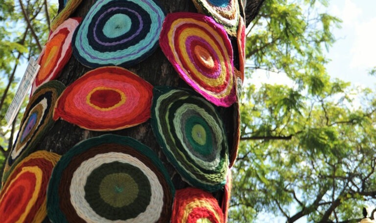 Viele bunte, selbstgemachte runde Sitzkissen hängen an einem Baum.
