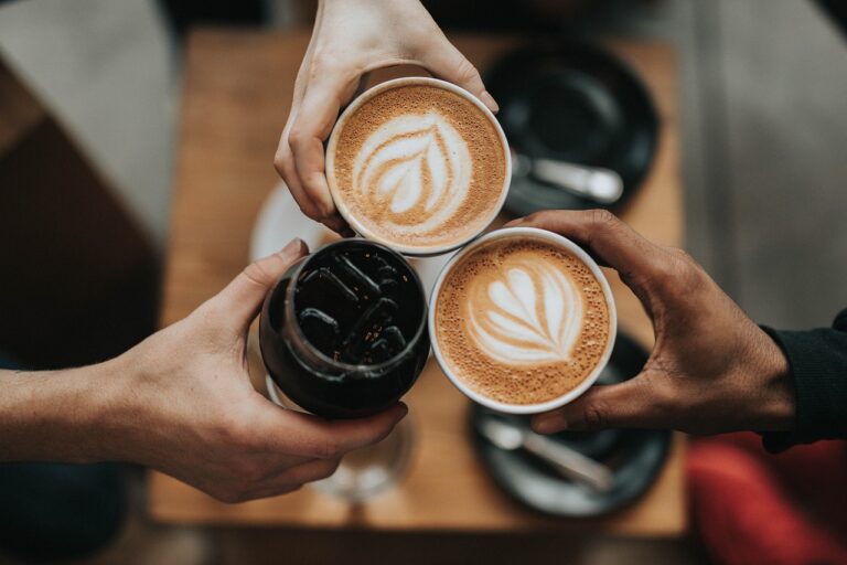 Tres manos sostienen cada una una taza de café.