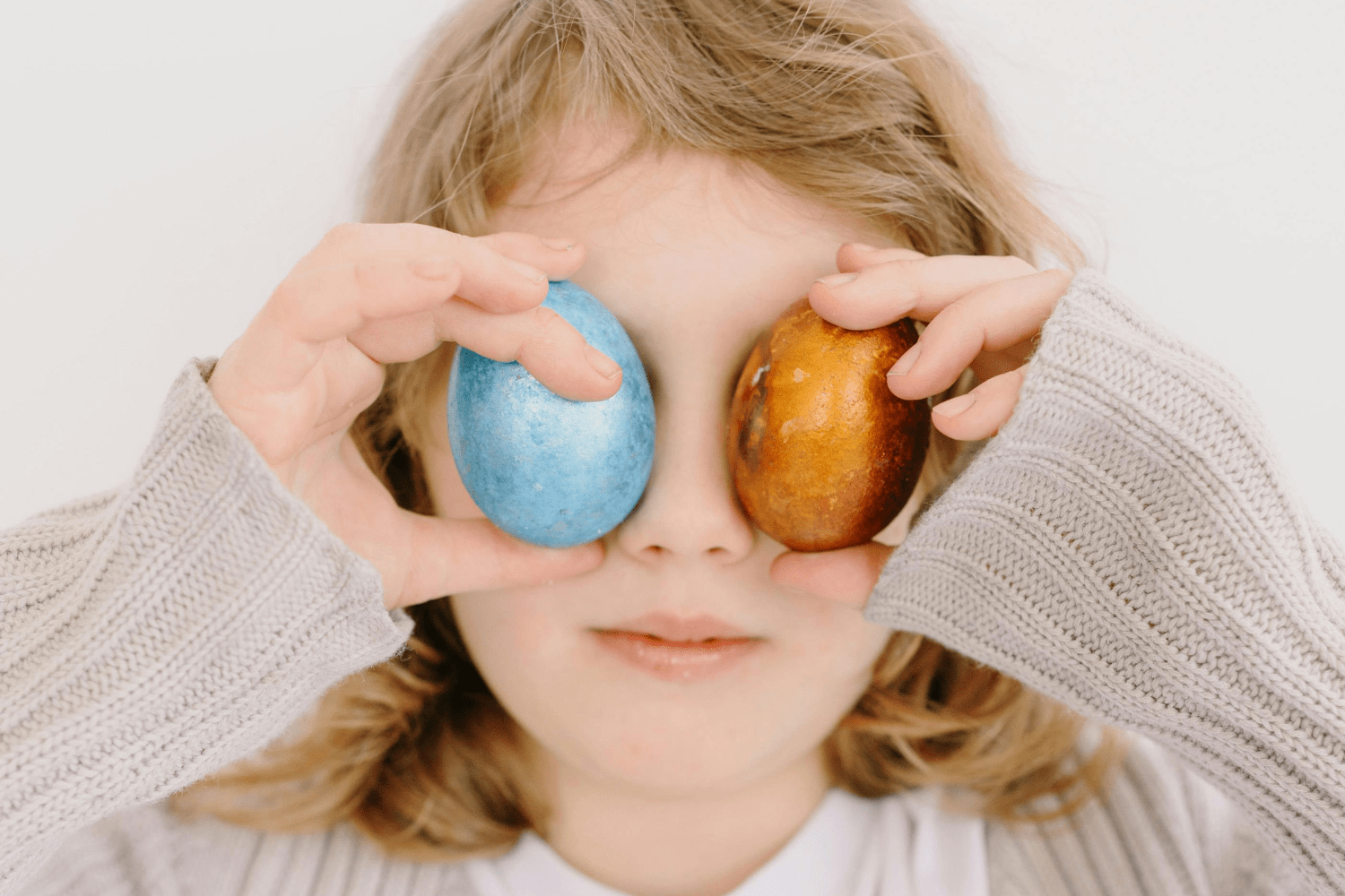 A child holds two Easter eggs in front of his eyes