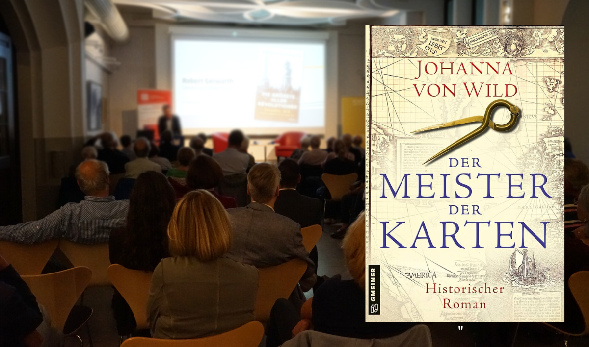 Das Buchcover "Der Meister der Karten" vor dem Hintergrund einer Veranstaltung.