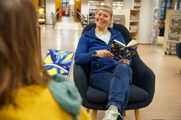 Una mujer se sienta frente a otras con un libro.