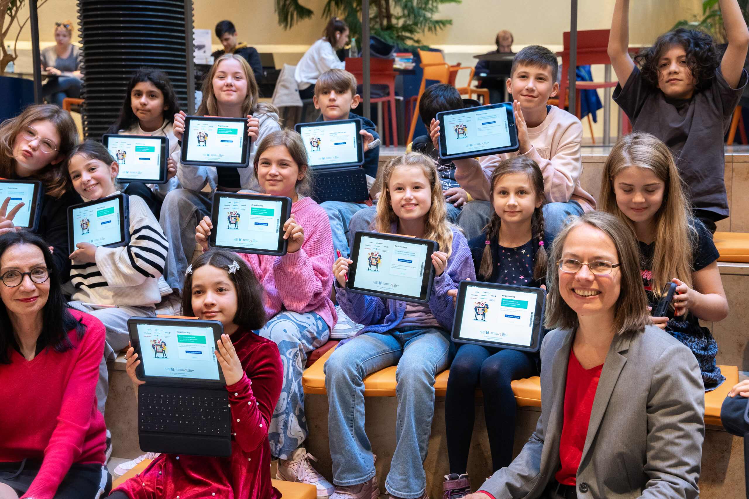 Children hold up tablets with the digital Bibcard, with Education Senator Aulepp sitting between them